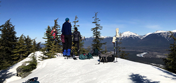 Couple of hikers atop a mountain looking across a snow covered valley
