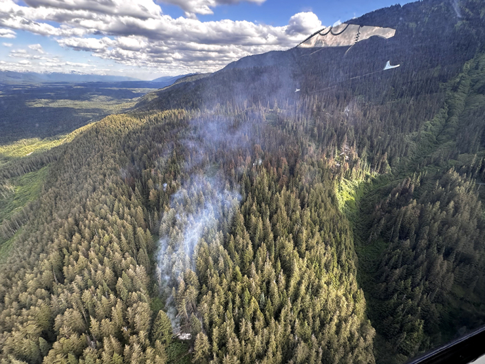 Mountain view of smoke rising out ot the forested slope.