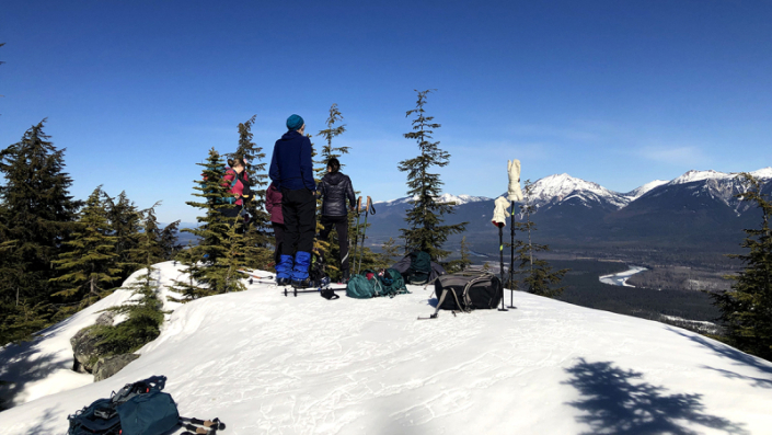 Couple of hikers atop a mountain looking across a snow covered valley